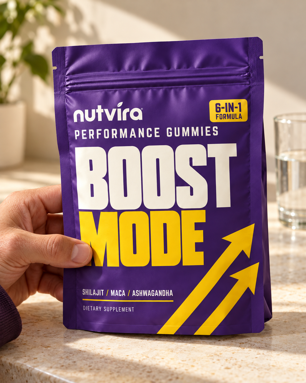 Nutvira Boost Mode purple and yellow resealable pouch held beside a glass of water in natural daylight.